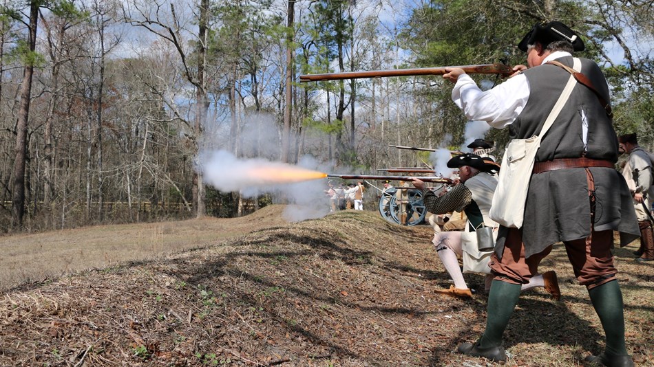 Patriot Militia fire their muskets from behind earthworks