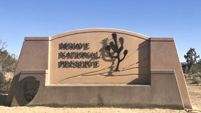 Mojave National Preserve Welcome Sign on Kelbaker Road with snow in the mountains on a cloudy day