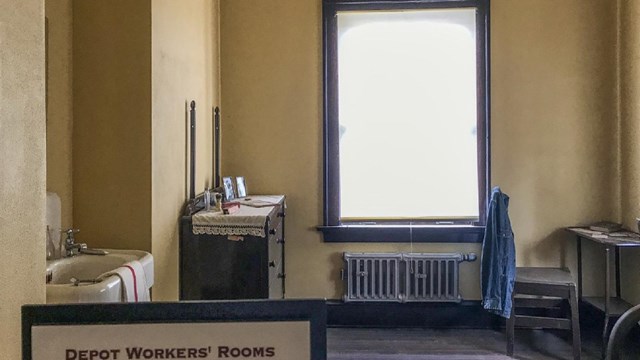 The historic workers room at Kelso Depot with a sink, dresser drawer, table,  chair, and a bed.