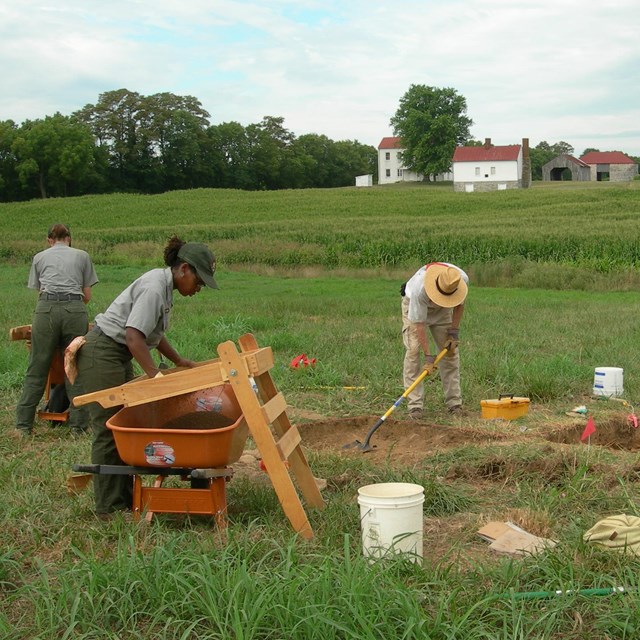 Archeologists sift soil and dig in the middle of a green field.
