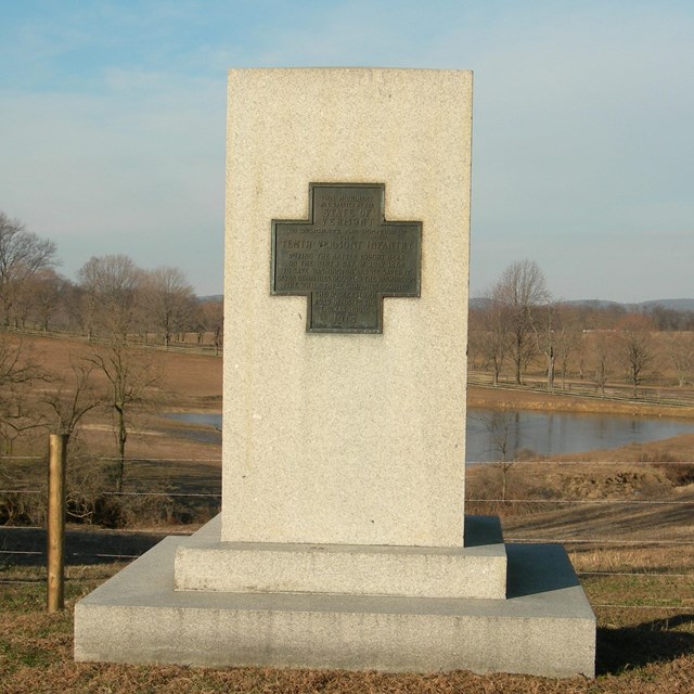 A tall rectangular stone with a bronze Greek Cross centered at the top.