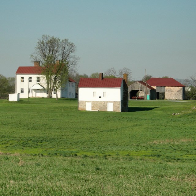 A farm house, small two-story building, and stone barn surrounded by green grassy fields.