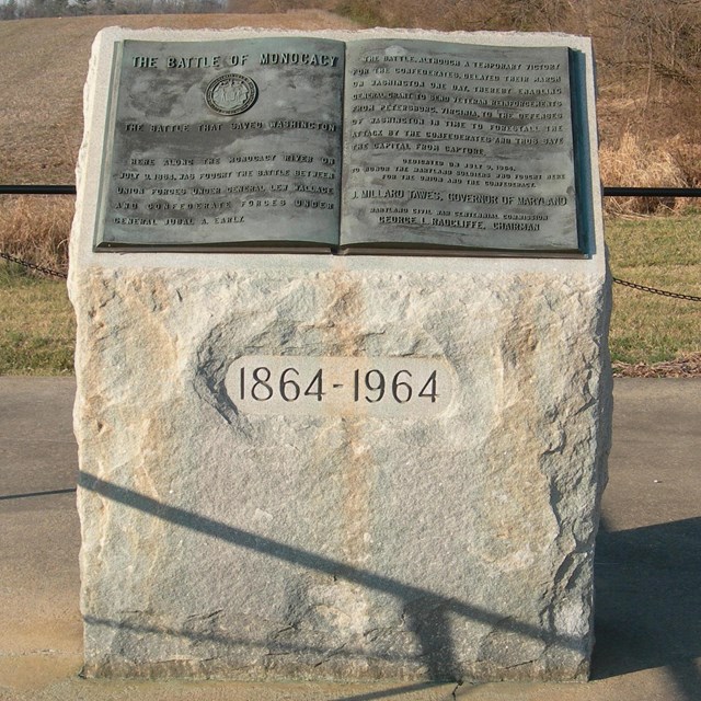 A rectangular stone block with an angled top. A bronze plaque in the shape of a book on the top.