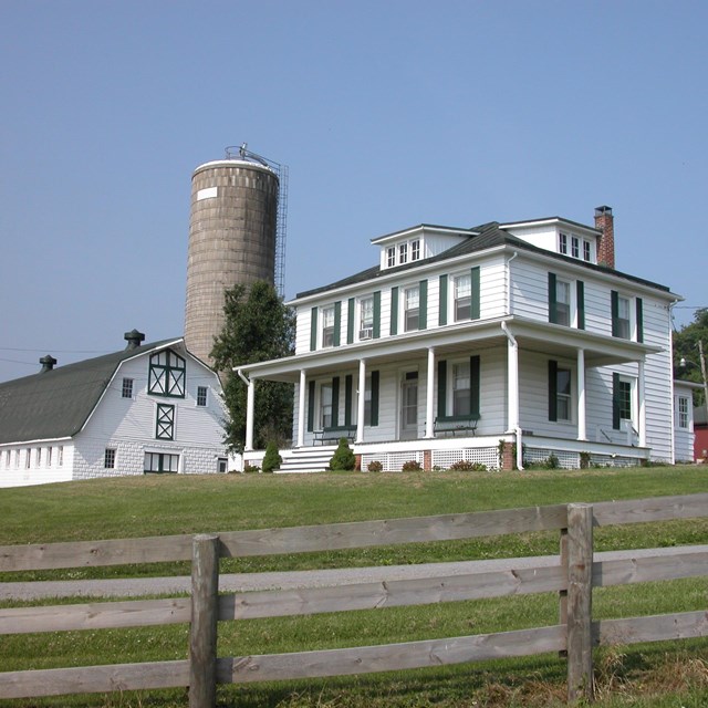 A two-story white farm house with a white barn and silo behind it.