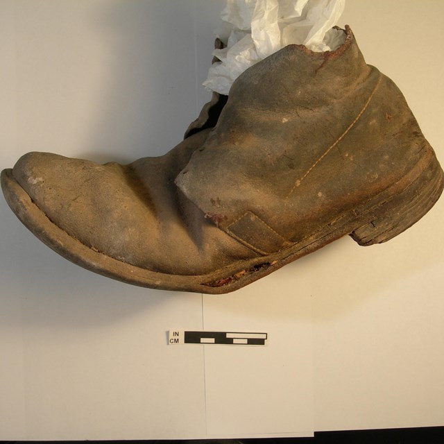 An old, brown leather shoe on a white background with a distance scale underneath it. 