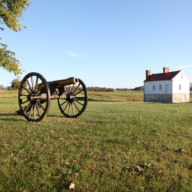 A cannon and a farm building in a field.