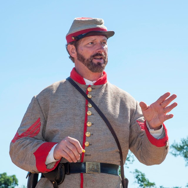 A man in a gray uniform with red trim tells a story.