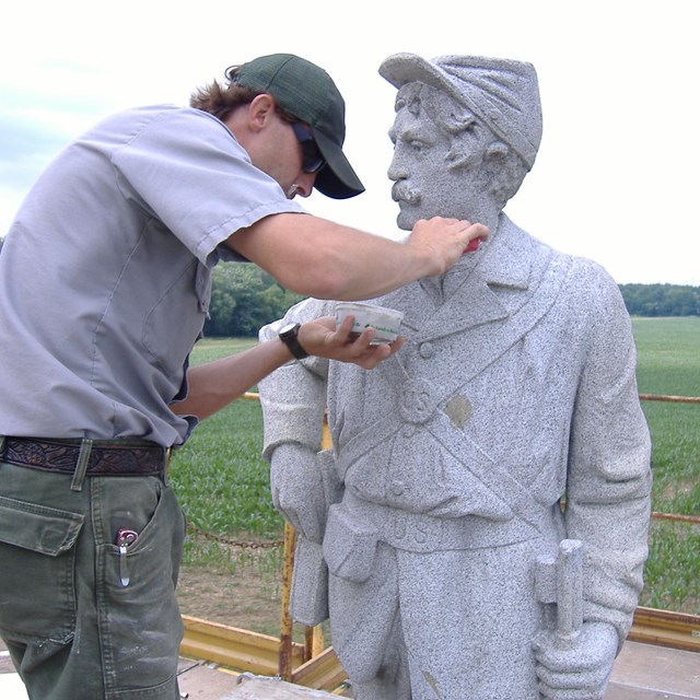 National Park Service employee cleans a stone statue of a Civil War soldier.