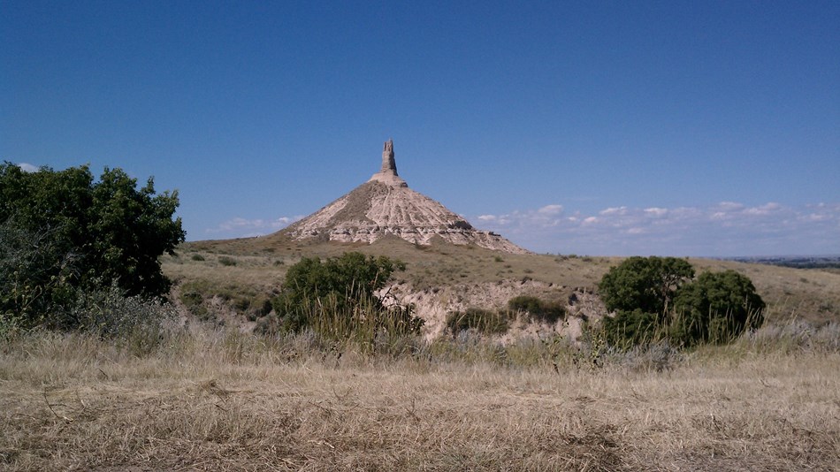 A pointed bluff landmark sticks out above a flat valley with large green shrubs.