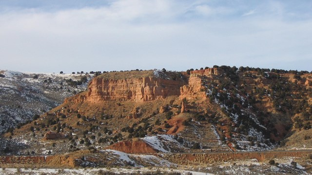 Towering sandstone cliffs, dusted with snow, line a canyon.