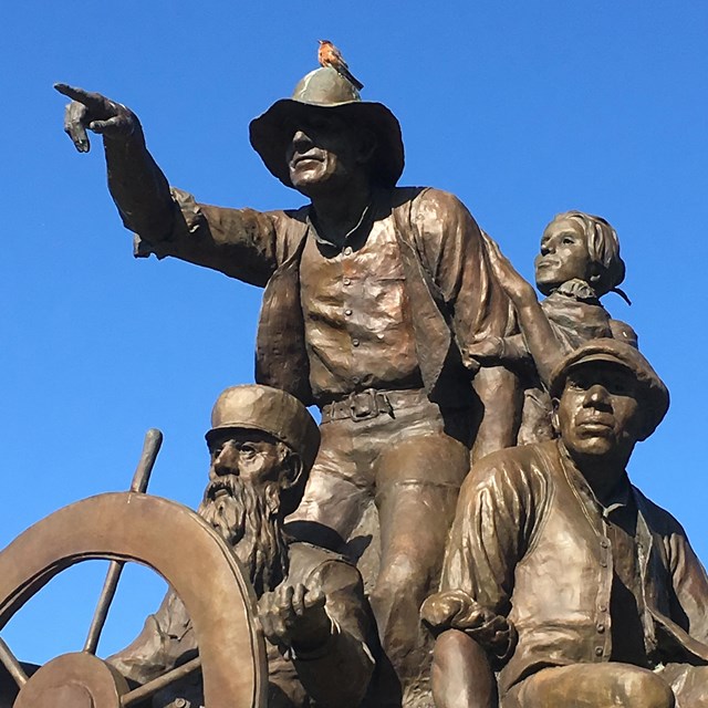 A bronze statue of a pioneer man pointing, surrounded by a few other pioneer men.