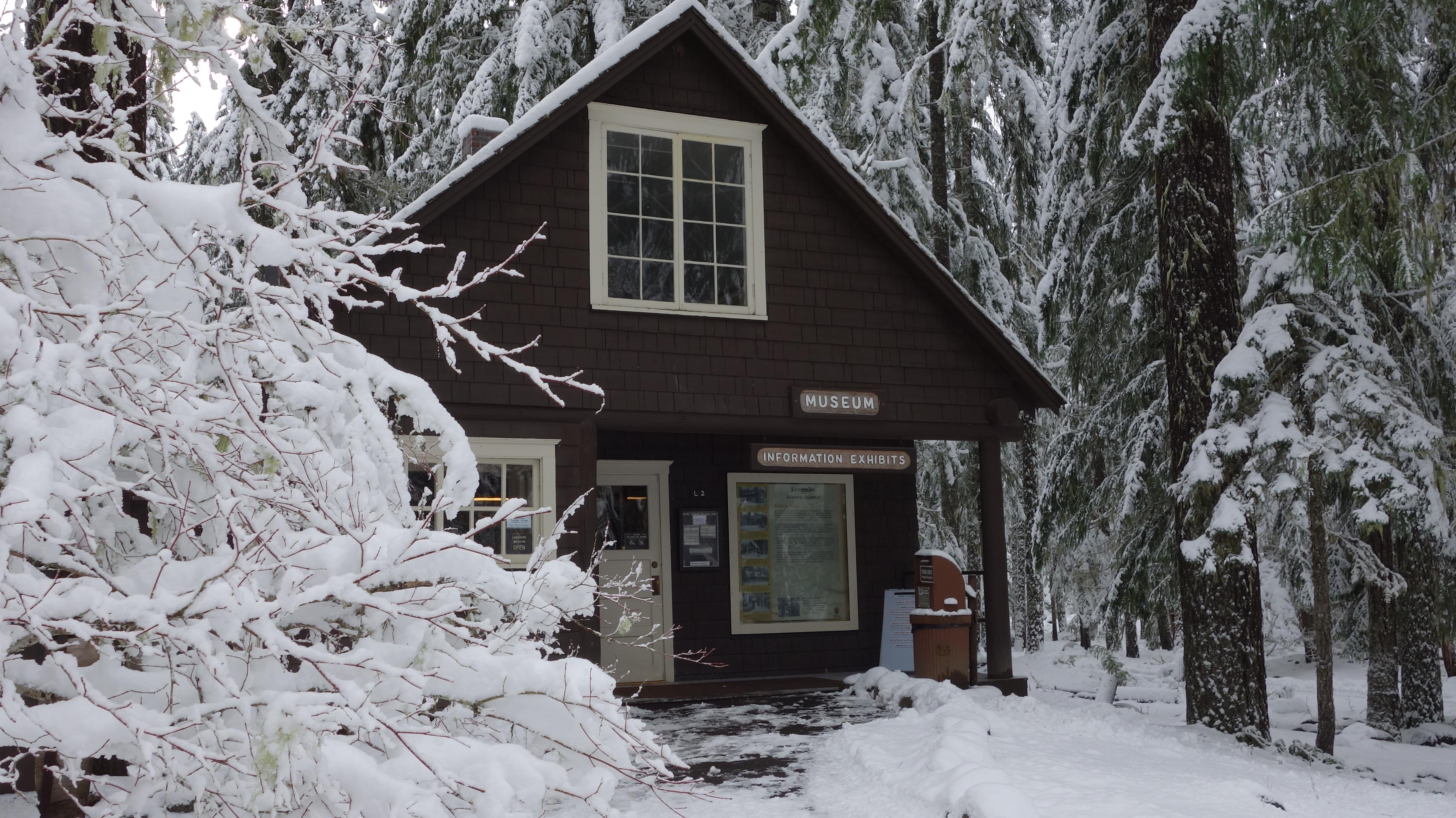 A small wood building framed by a snowy forest. 