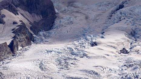 A glacier broken by crevasses on a rocky mountain slope. 