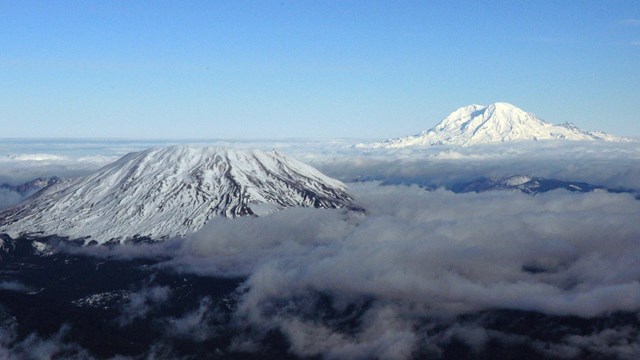 Two snowy volcanic peaks, one with the top cratered, rise above the landscape. 