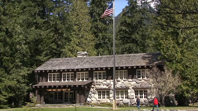 A two story rock and wood building surrounded by forest. 