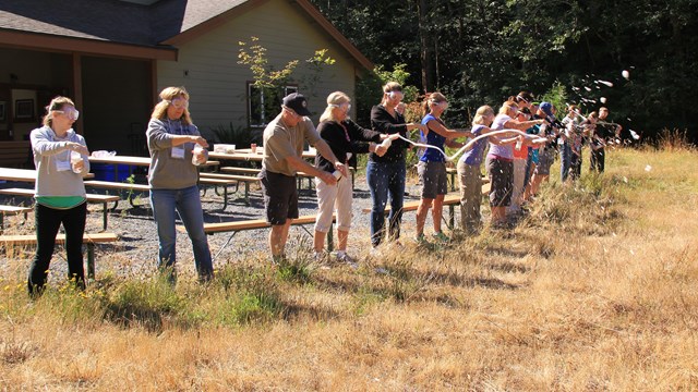 A ring of teachers in safety goggles hold soda bottles spouting foam "eruptions". 