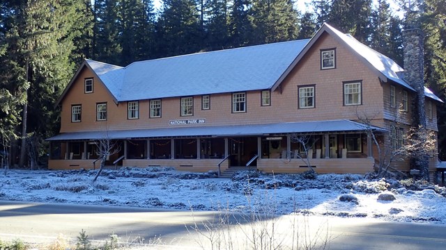 A two-story wood building with a covered porch dusted in snow.