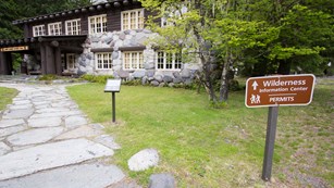 A sign next to a path leading to a rustic building reads 