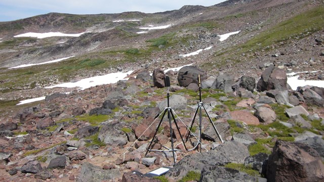 Two tripods with microphones set up on a rocky subalpine slope.