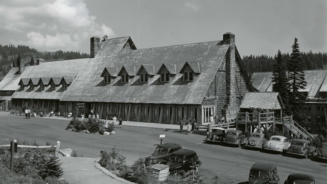 A large wood building with a shingle roof, gabled windows, stone fireplace and large parking lot.
