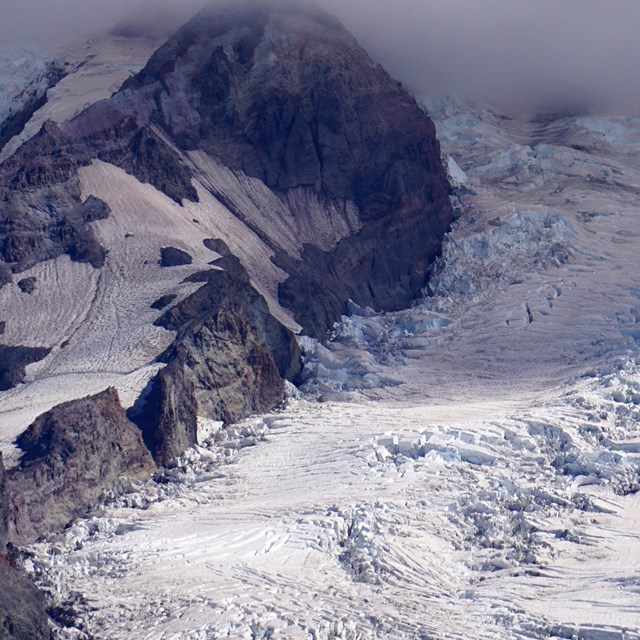 A glacier broken by crevasses on a rocky mountain slope. 