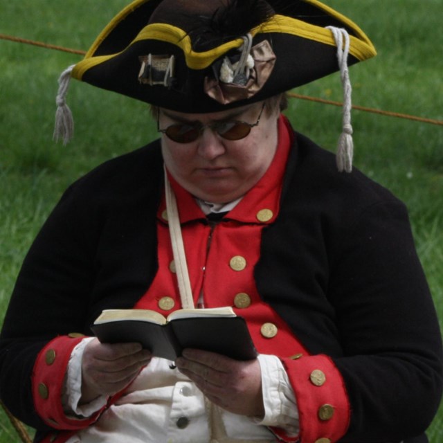 A man in Continental soldier uniform reads a book