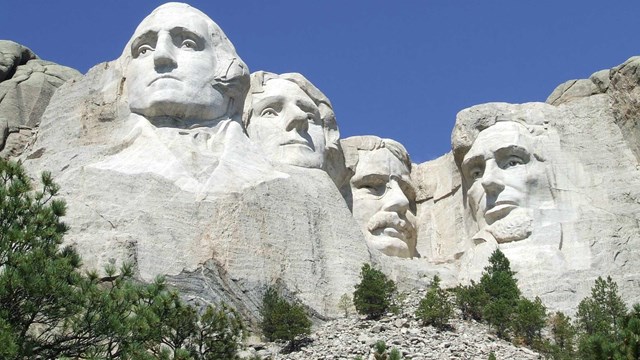 Mount Rushmore viewed from the Presidential Trail under a clear blue sky.