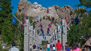 Visitors walking along the Avenue of Flags with Mount Rushmore in the background.