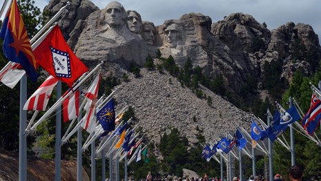 Visitors walking along the Avenue of Flags with Mount Rushmore in the background.