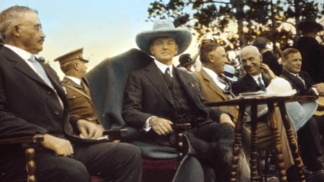 President Calvin Coolidge (center) sits next to Senator Peter Norbeck (left) at the 1927 dedication.