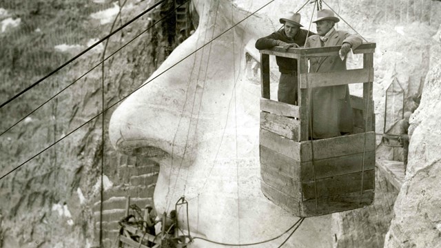 Lincoln Borglum and Gutzon Borglum in tram car with Thomas Jefferson sculpture in the background.