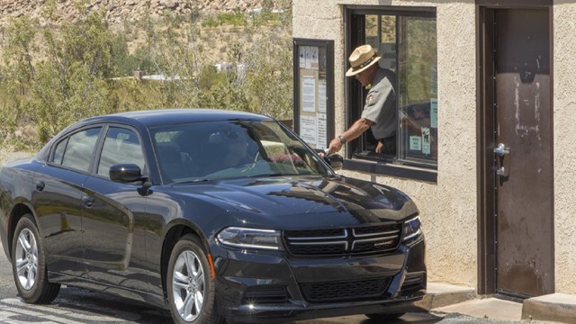 Ranger at an entrance station handing a driver a brochure