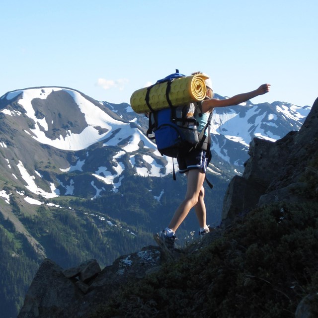 Hiker with full backpack walks along mountain ridge.
