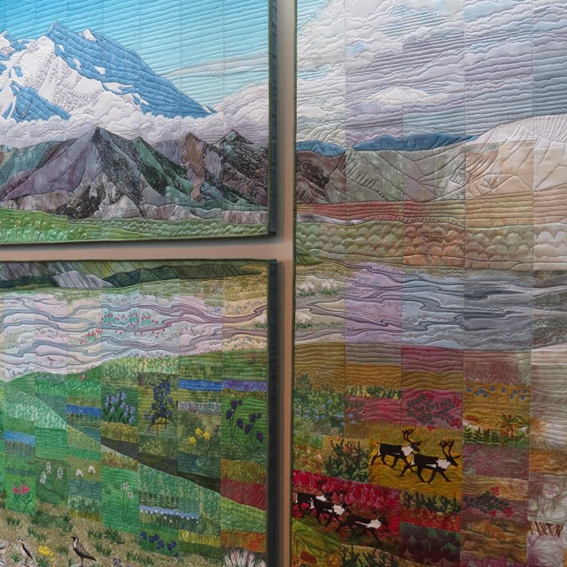 Panels of a large quilt on the wall showing scenes from a mountain landscape.