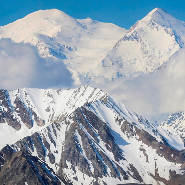 A large snow-covered mountain with clouds obscuring its top half.