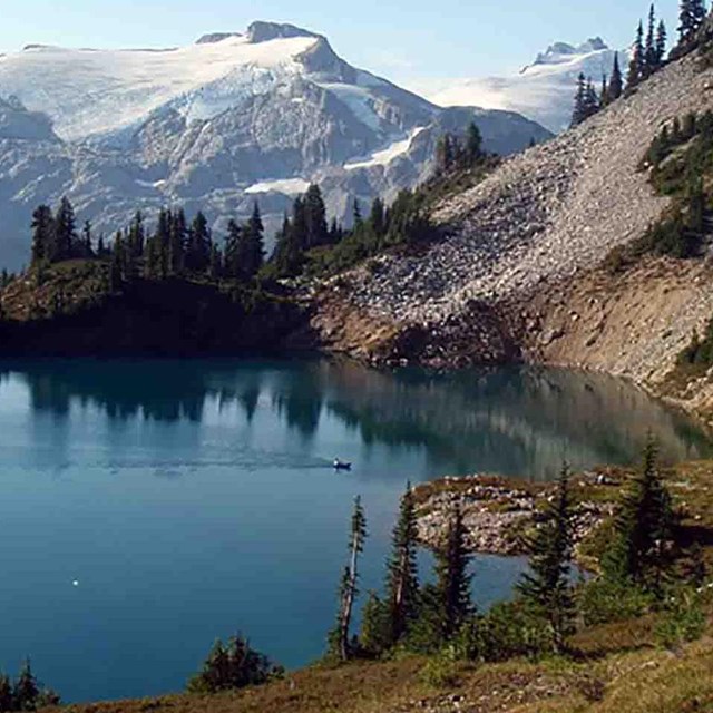 A crystal blue alpine lake with steep, forested cliffs and a small boat on the water.