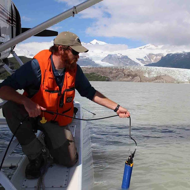 A researcher collects water quality data from a plane's float in the middle of a lake.