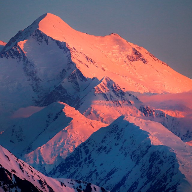 A mountain peak covered in snow, with an orange glow
