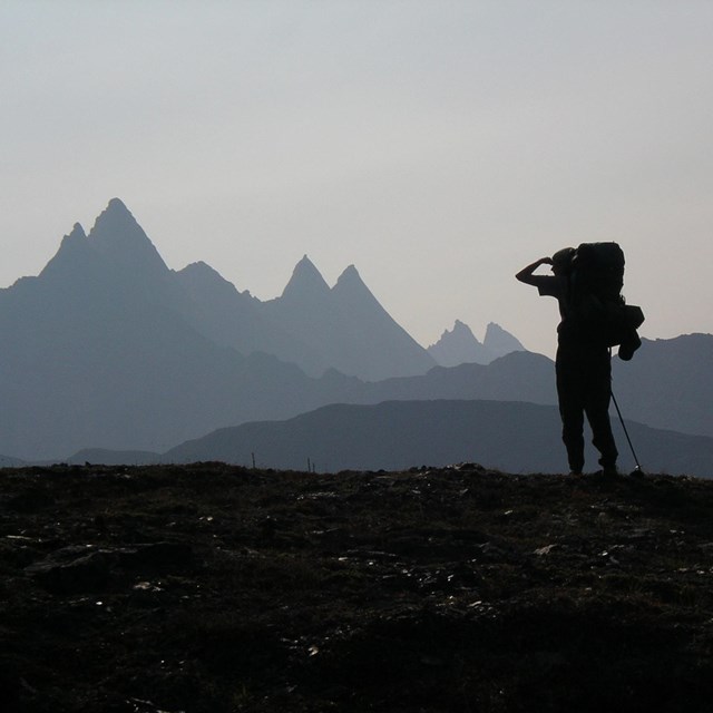 The silhouette of a person with backpack looking at sharp, steep, peaks in a haze.