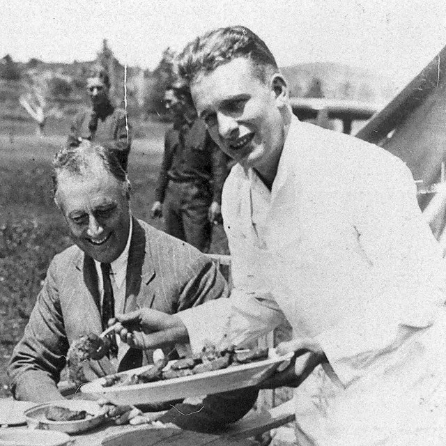 Black and white image men sitting at an outdoor table with one young server.