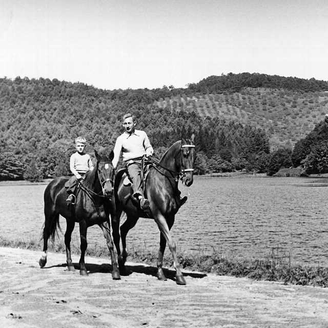 Two people, one older and one a child, on horseback in a black and white image.