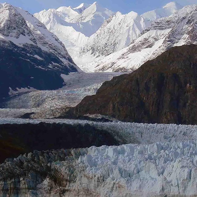 A large glacier cascades from the mountains to the coast.