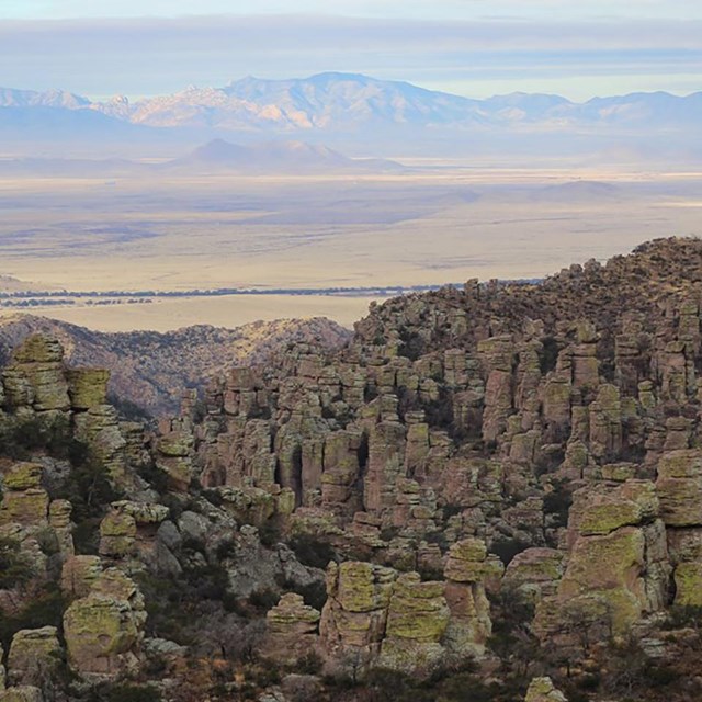 Looking across rhyolite rock formations to a sea of dry desert and distant mountains
