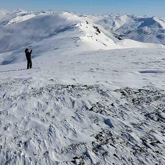 a researcher monitors snow on a wind-swept mountain ridge.