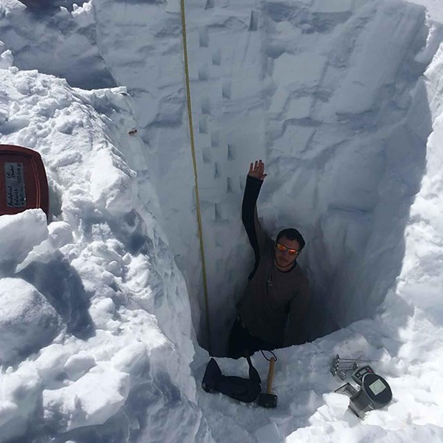 A researcher stands in a deep snow pit where he is collecting chemistry data.