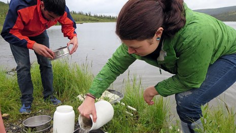 two researchers use equipment by a river