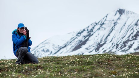 a woman kneels in front of a snowy mountain to take a picture