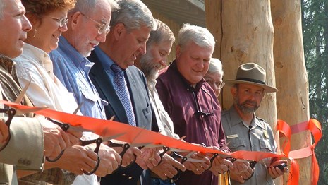 a line of people hold scissors to a ribbon in front of a building