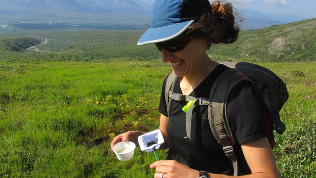 woman holding a bug net a cup outside