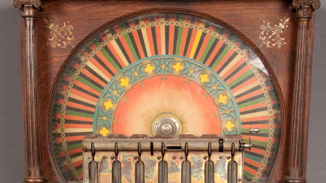 Wood cabinet 5 ft. 10 in. high. Colored wheel with wagers 10c to $5.  In front: Slots for 7 coins, c